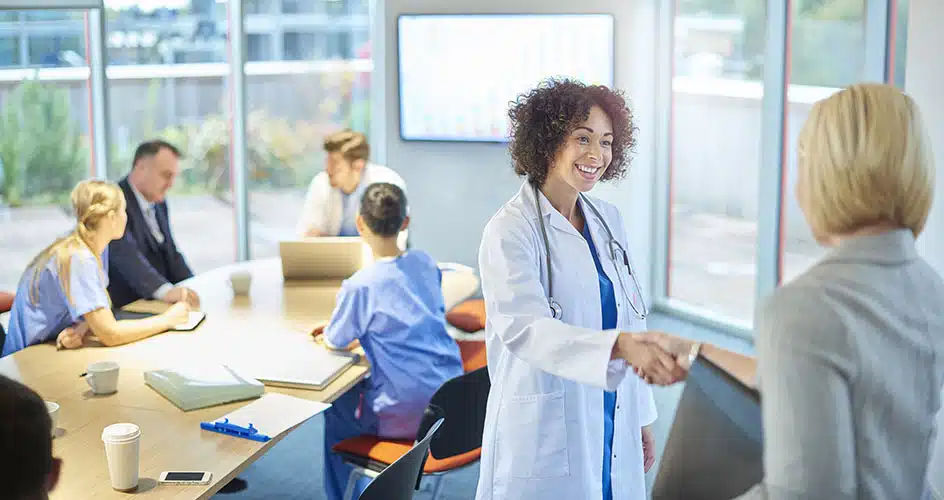 a businesswoman chats with a doctor as they leave a boardroom meeting in a hospital